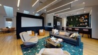 Located at 1000 Old Brook Rd in Charlottesville, Virginia, this single-floor amenity facility is thoughtfully designed to offer a comprehensive and modern community experience. The centerpiece of the space is a spacious lounge area featuring bold navy and teal accents, sleek linear LED ceiling lighting, warm hardwood flooring, and an inviting arrangement of contemporary sofas and accent chairs atop a vibrant geometric rug. Large floor-to-ceiling windows flood the lounge with natural light and provide open views of the surrounding outdoor deck and landscape. Adjacent to the lounge is a stylish kitchenette and bar area, highlighted by a striking hexagonal green tile backsplash, open shelving, white quartz countertops, pendant lighting, and a bar-height island with seating — ideal for socializing. Private meeting and conference areas with glass-paneled sliding doors and marble-top tables offer quiet, functional spaces for work or small gatherings. The well-appointed fitness center is equipped with a comprehensive selection of Life Fitness cardio machines, selectorized weight equipment, a cable machine system, mirrored walls, and a ceiling fan, all set against deep teal accent walls. Dual-height drinking fountains with a bottle-filling station provide convenient hydration throughout the facility.