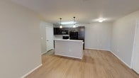 This single-story residence is designed with a modern, functional layout that seamlessly connects the kitchen and living areas. The open-concept kitchen serves as a central feature, equipped with dark espresso-toned cabinetry, black appliances including a refrigerator, range, and over-the-range microwave, and a white countertop peninsula that doubles as a prep and dining surface. Pendant lighting hangs above the peninsula, adding a decorative touch while enhancing task lighting. A double sink is integrated into the extended countertop run along the kitchen's perimeter.

Light wood-style plank flooring extends throughout the main living areas, contributing to a cohesive and contemporary aesthetic. The living area is bright and open, with a ceiling fan and access to an outdoor area through double French doors fitted with blinds. A secondary room features a window with natural light and its own ceiling fan fixture.

Two bathrooms serve the space: one includes a full tub-shower combination with white surround and recessed lighting, while the other offers an elongated double-sink vanity with dark cabinetry, a large mirror, and wood-style flooring. Neutral gray-toned walls throughout create a clean, move-in-ready atmosphere.