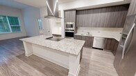 Located at 350 Village Drive in King of Prussia, PA, this thoughtfully designed 2-bedroom, 2-bathroom residence offers a comfortable and modern living experience across a single floor. The open-concept kitchen is a standout feature, showcasing dark wood-grain cabinetry, stainless steel appliances including a built-in oven, microwave, dishwasher, and French door refrigerator, all complemented by a large granite-topped island with a sleek island hood. Light wood-style flooring ties the kitchen and adjacent living areas together seamlessly. The primary bedroom is generously sized, featuring an elegant tray ceiling with a ceiling fan and plush carpeting. It connects to a spacious walk-in closet with built-in wire shelving and a luxurious en-suite bathroom appointed with marble-style tile, a soaking tub, a glass-enclosed shower, granite countertops, and dark wood vanity cabinetry. The second bedroom also features a tray ceiling, ceiling fan, carpeted floors, and a large window overlooking lush greenery. The second bathroom mirrors the refined finishes found throughout, with marble tile flooring, a granite vanity, and gold-framed mirror. Two well-sized closets provide ample storage throughout the residence.