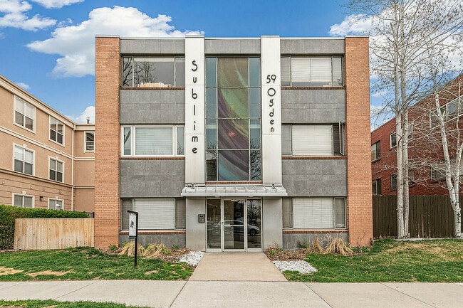 Modern apartment exterior of Sublime 59, showcasing chic architecture with contrasting brick and concrete facade under a vibrant blue sky. - Sublime