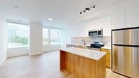 Located at 1600 James Naismith Drive in Ottawa, Ontario, this thoughtfully designed one-bedroom, one-bathroom unit offers a clean, contemporary aesthetic throughout. Light hardwood flooring flows seamlessly across the entire space, complementing the bright white walls and creating a cohesive, modern atmosphere.

The open-concept kitchen is a standout feature, showcasing a two-tone design with warm natural wood lower cabinetry and crisp white upper cabinets. A quartz-topped kitchen island provides additional workspace and a natural gathering point. The kitchen is equipped with a full suite of stainless steel appliances, including a dishwasher, electric range, over-the-range microwave, and refrigerator, all set against a soft grey subway tile backsplash.

The living area flows naturally from the kitchen, bathed in natural light from large floor-to-ceiling windows that frame views of the surrounding Ottawa neighbourhood and greenery.

The bedroom is a well-proportioned, quiet retreat featuring large windows that continue the theme of natural light, along with a built-in sliding door closet for practical storage.

The bathroom is finished with crisp white vertically-stacked tile surrounding a soaker tub and shower combination, accented by sleek matte black fixtures. A clean, bright hallway connects all rooms efficiently, completing this well-appointed unit.