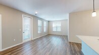 This single-floor space is designed with a clean, contemporary aesthetic throughout. The open living area is bright and welcoming, featuring durable wood-look flooring and multiple windows fitted with white horizontal blinds that allow generous natural light to fill the room. A glass-paneled exterior door provides additional light and outdoor access.

The kitchen is a standout feature, outfitted with crisp white shaker-style cabinetry, matte black hardware, and white quartz countertops. A classic subway tile backsplash adds texture, while a full suite of stainless steel appliances—including a refrigerator, range, built-in microwave, and dishwasher—ensures full functionality. A central island with a sink provides additional workspace and storage.

The bedrooms are carpeted for comfort and feature neutral walls, allowing for versatile use. Each room benefits from multiple windows that bring in natural light. The bathrooms maintain the space's modern palette, with white shaker vanities, quartz countertops, matte black hardware, and wood-look flooring. One bathroom includes a full tub-shower combination, while another offers a more streamlined half-bath configuration. Overall, the space presents a cohesive, move-in-ready environment.