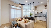 This thoughtfully designed single-floor residence offers a seamless blend of modern style and functional living. A welcoming entryway corridor, accented by a gallery of arched mirrors, leads into the expansive open-concept living and dining area. The living room impresses with soaring ceilings, light wood flooring, and generous natural light streaming through large windows dressed with clean white blinds. A sleek ceiling fan anchors the space above a comfortable sectional sofa.

The kitchen is well-equipped with white shaker cabinetry extending to the ceiling, dark granite countertops, a classic subway tile backsplash, and stainless steel appliances. A central island with bar seating and pendant lighting serves as a natural gathering point, flowing effortlessly into the adjacent dining area bathed in light from a striking bay window arrangement.

The bedroom offers a serene retreat with plush carpeting, large windows, and ample closet space. The bathrooms are finished with granite-topped vanities, large framed mirrors, and white subway tile tub surrounds. Throughout the residence, a cohesive neutral palette, elevated ceilings, and carefully considered finishes create a bright, airy, and inviting atmosphere.