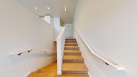 Located in Seattle's vibrant Eastlake neighborhood, this two-story residence offers a thoughtfully designed 1-bedroom, 2-bathroom layout across two distinct levels. Light-toned hardwood-style flooring flows consistently throughout both floors, complementing the clean white walls and recessed lighting that give the home a bright, modern feel.

The main level houses the kitchen, which is a standout feature of the space. It is outfitted with white shaker-style cabinetry, open wood-toned shelving, a white tile backsplash, light quartz countertops, and a full suite of stainless steel appliances including a range, refrigerator, dishwasher, and microwave. A large window floods the kitchen and living area with natural light and provides views of the surrounding greenery.

A striking staircase with warm wood-toned treads, white risers, and a sleek white railing connects both floors. The upper level hosts the primary bedroom, which is equipped with a wall-mounted mini-split system for climate control and features a horizontal window that brings in natural light. A dedicated closet and hallway provide additional functionality.

Both bathrooms are finished in a clean, contemporary style with white subway tile tub-shower surrounds, chrome fixtures, and wood-style flooring, offering a cohesive and polished aesthetic throughout.