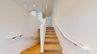 Located in Seattle's vibrant Eastlake neighborhood, this two-story residence offers a thoughtfully designed 1-bedroom, 2-bathroom layout across two distinct levels. Light-toned hardwood-style flooring flows consistently throughout both floors, complementing the clean white walls and recessed lighting that give the home a bright, modern feel.

The main level houses the kitchen, which is a standout feature of the space. It is outfitted with white shaker-style cabinetry, open wood-toned shelving, a white tile backsplash, light quartz countertops, and a full suite of stainless steel appliances including a range, refrigerator, dishwasher, and microwave. A large window floods the kitchen and living area with natural light and provides views of the surrounding greenery.

A striking staircase with warm wood-toned treads, white risers, and a sleek white railing connects both floors. The upper level hosts the primary bedroom, which is equipped with a wall-mounted mini-split system for climate control and features a horizontal window that brings in natural light. A dedicated closet and hallway provide additional functionality.

Both bathrooms are finished in a clean, contemporary style with white subway tile tub-shower surrounds, chrome fixtures, and wood-style flooring, offering a cohesive and polished aesthetic throughout.