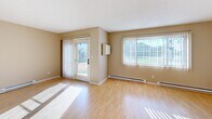 This single-floor residence offers a thoughtfully laid-out interior finished in warm, neutral tones throughout. The spacious living area features light hardwood flooring, a ceiling fan, and large windows fitted with vertical blinds that invite generous natural light. Sliding glass doors provide direct outdoor access, enhancing the open, airy feel of the main living space. Baseboard heating is present throughout the unit, ensuring consistent warmth.

The galley-style kitchen is outfitted with white cabinetry, a double stainless steel sink, laminate countertops, and a full suite of white appliances including an electric range, refrigerator, and over-the-range microwave. Hardwood flooring continues through the kitchen, which connects directly to a dedicated laundry room equipped with a full-size washer and dryer, overhead storage cabinets, and a water heater.

The bedrooms are carpeted and comfortably sized, each featuring baseboard heating and windows with blinds. At least one bedroom includes a closet with paneled double doors. The bathroom is cleanly finished with tile flooring, a tub-shower combination with tiled surround, a toilet, a vanity with storage, and a chrome grab bar. Textured ceilings are found in several rooms, adding a classic touch to the overall design.