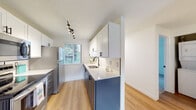 This single-floor unit offers a thoughtfully updated interior with a clean, modern aesthetic throughout. The open-concept layout connects the living area to the kitchen, creating a functional and cohesive flow. Warm hardwood-style flooring runs through the main living spaces, complemented by crisp white walls and a textured ceiling.

The kitchen is a standout feature, showcasing a striking two-tone design with white upper cabinetry fitted with matte black hardware and navy blue lower cabinets. Light quartz countertops provide a bright contrast, while a window above the sink fills the space with natural light and greenery views. Stainless steel appliances, including a range, over-the-range microwave, and refrigerator, complete the well-equipped galley-style kitchen.

The spacious living room extends to a sliding glass door that opens to a balcony, allowing abundant natural light and outdoor views. A ceiling fan with integrated lighting adds both comfort and function to the space.

The bedroom features plush carpeting, offering a soft and comfortable retreat. The bathroom is finished in a clean, contemporary style, featuring a round mirror with a dark frame, a undermount sink with a gray vanity, and a full tub and shower combination with updated fixtures.