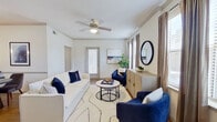 This single-story residence presents a cohesive, well-designed interior centered around a navy blue and neutral color palette throughout. The living room serves as the heart of the space, featuring crown molding, wood-look flooring, and a ceiling fan overhead. Multiple windows fitted with blinds and draping curtains allow natural light to filter in, creating a bright and welcoming atmosphere. A panel door provides access to an exterior area, adding convenience to the layout.

Adjacent to the living room, a compact dining area accommodates a round table and seating, separated by a partial wall adorned with framed artwork. The kitchen is equipped with dark espresso-toned cabinetry, granite countertops, stainless steel appliances including a refrigerator, range, and microwave, and track lighting above. A double sink anchors the workspace.

The bedroom features a soothing slate-blue accent wall, a ceiling fan, and generous windows that bring in ample natural light. A spacious walk-in closet with dual hanging rods and shelving provides substantial storage. The full bathroom includes a tub-shower combination, wood-look flooring, and dark vanity with granite countertops, completing this well-organized and cohesive residence.