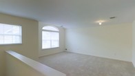This single-floor space presents a spacious, open room characterized by its bright and neutral aesthetic. The most notable architectural feature is a prominent arched window, which anchors one wall and allows generous amounts of natural light to fill the interior, creating an airy and welcoming atmosphere. The window's classic arched transom adds a touch of architectural elegance to an otherwise understated space.

The room is finished with wall-to-wall carpeting in a soft, neutral tone that complements the cream-colored walls, contributing to the overall sense of warmth and cohesion. The smooth white ceiling is accented by a flush-mounted ceiling light, providing practical overhead illumination. Visible HVAC vents indicate a climate control system integrated into the ceiling design.

The walls are clean and unadorned, offering versatility for various uses and furnishing arrangements. The generous proportions of the room provide ample space for a range of configurations. Overall, the space conveys a calm, move-in-ready environment defined by its simplicity, natural light, and functional design.