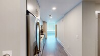 Located in the heart of downtown Raleigh on Fayetteville Street, this one-bedroom, one-bathroom residence offers a modern and efficient layout with clean, contemporary finishes throughout. The living room is bathed in natural light thanks to expansive floor-to-ceiling windows that frame impressive city skyline views, creating an open and airy atmosphere. Light gray wood-tone flooring runs throughout the space, complementing the neutral white walls and adding a cohesive, polished feel. A ceiling fan adds both function and style to the living area. The bedroom continues the floor-to-ceiling window theme, flooding the room with light and views, while a distinctive sliding barn-style door adds a modern design touch and leads to the closet. The bathroom is well-appointed with a wood-grain vanity featuring gold hardware, a white quartz countertop, a large mirror, and a soaking tub with a tiled surround and brushed nickel fixtures. The hallway connects all areas efficiently, and the overall layout makes excellent use of the available space. This residence offers a sophisticated urban living experience in one of Raleigh's most walkable and vibrant downtown locations.