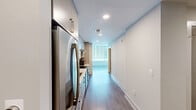 Located in the heart of downtown Raleigh on Fayetteville Street, this one-bedroom, one-bathroom residence offers a modern and efficient layout with clean, contemporary finishes throughout. The living room is bathed in natural light thanks to expansive floor-to-ceiling windows that frame impressive city skyline views, creating an open and airy atmosphere. Light gray wood-tone flooring runs throughout the space, complementing the neutral white walls and adding a cohesive, polished feel. A ceiling fan adds both function and style to the living area. The bedroom continues the floor-to-ceiling window theme, flooding the room with light and views, while a distinctive sliding barn-style door adds a modern design touch and leads to the closet. The bathroom is well-appointed with a wood-grain vanity featuring gold hardware, a white quartz countertop, a large mirror, and a soaking tub with a tiled surround and brushed nickel fixtures. The hallway connects all areas efficiently, and the overall layout makes excellent use of the available space. This residence offers a sophisticated urban living experience in one of Raleigh's most walkable and vibrant downtown locations.
