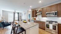 This well-designed single-floor residence offers a cohesive blend of modern finishes and comfortable living spaces. The open-concept kitchen is a standout feature, showcasing rich walnut-toned cabinetry, granite countertops, a white subway tile backsplash, and a full suite of stainless steel appliances including a gas range, built-in microwave, refrigerator, and dishwasher. A generously sized kitchen island with seating serves as both a functional workspace and a social hub. Pendant lighting overhead adds a warm, inviting touch. The adjoining living area features light hardwood flooring throughout, a ceiling fan, and a striking tropical botanical mural accent wall that lends a distinctive character to the space. Natural light pours in through large windows dressed with layered blinds and curtains. Two bedrooms offer restful retreats, each with its own color palette and large windows. One bedroom connects directly to a full bathroom and a spacious walk-in closet equipped with built-in shelving and hanging rods. The bathroom features a soaking tub and wood-toned vanity with granite countertops. Every room reflects a thoughtful, contemporary design sensibility with consistent hardwood-style flooring tying the entire residence together.