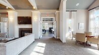 Located at 1 Seven Springs Lane in Burlington, MA, this single-floor community clubhouse is thoughtfully designed to offer a range of social and recreational spaces within a refined, welcoming environment. The main lounge area is anchored by a sleek fireplace topped with a large wall-mounted television, flanked by white fluted columns and surrounded by plush velvet seating. Soaring vaulted ceilings with exposed beams and track lighting add architectural drama, while large windows and French doors flood the space with abundant natural light. Adjacent to the lounge, a bright and airy sitting room features cathedral ceilings, sheer floor-to-ceiling drapery, a built-in window seat, and a casual dining table — ideal for relaxed conversation or small gatherings. A dedicated conference and meeting room offers a formal rectangular table surrounded by upholstered chairs, flanked by built-in display cabinetry finished in soft blue, and accented by a curated gallery wall. The game room provides a lively contrast, with rich hardwood flooring, a pool table, lounge seating, pendant lighting, ceiling fans, and a bar counter area with additional seating. Throughout, the space maintains a consistent palette of warm neutrals, crisp white millwork, and soft blue accents, creating a cohesive and sophisticated ambiance.