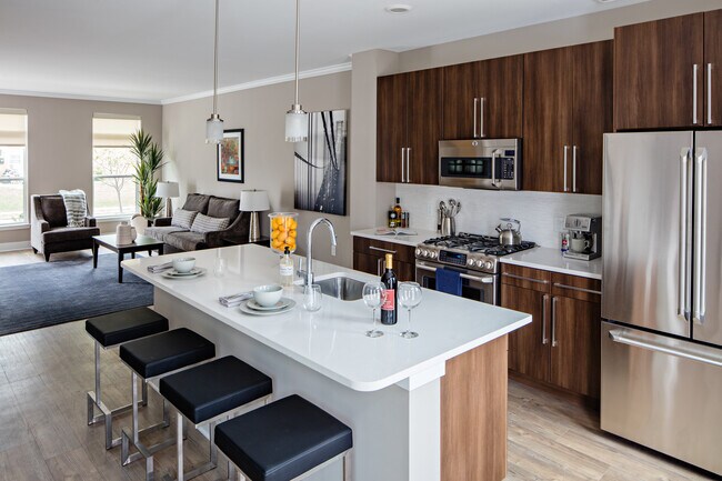 Cocina de la colección Signature de Townhome con gabinetes de roble, encimeras de cuarzo gris claro, salpicadero de azulejos blancos y pisos de superficie dura. Electrodomésticos de acero inoxidable de alta gama y refrigerador de puerta francesa. - Avalon Princeton