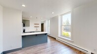 Located at 1216 N Superior St in Spokane, WA, this one-bedroom, one-bathroom unit offers a thoughtfully designed layout with modern finishes throughout. The open-concept kitchen and living area serves as the heart of the space, featuring slate-blue cabinetry, white quartz countertops, a peninsula with bar seating, stainless steel appliances including a refrigerator, range, microwave, and dishwasher, as well as warm wood floating shelves and a deep stainless steel sink. Light wood-tone luxury vinyl plank flooring runs throughout the entire unit, providing a clean, cohesive aesthetic. Large double-hung windows in the living area flood the space with natural light and offer views of the surrounding neighborhood greenery. The bedroom is a cozy, well-proportioned room with its own large window, a sliding closet with built-in shelving, and continued access to natural light. The bathroom is finished in a clean, minimalist style with gray cabinetry, a white vanity, and a full tub-shower combination. A dedicated closet provides additional storage. The unit's crisp white walls, recessed lighting, and consistent use of gray-blue accent tones throughout create a modern and cohesive living environment.