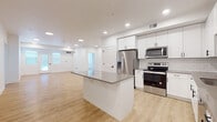 This single-floor unit presents a clean, contemporary design with a cohesive neutral color palette throughout. The open-concept kitchen and living area serves as the central hub of the space, anchored by a large center island with a dark quartz countertop that provides ample workspace and seating. The kitchen is well-appointed with white shaker-style cabinetry, a white subway tile backsplash, stainless steel appliances including a French door refrigerator with ice and water dispenser, an electric range, and an over-the-range microwave. Light wood-look flooring extends throughout the kitchen and living area, contributing to the bright, airy atmosphere enhanced by recessed lighting. The spacious living area offers generous room for various furniture arrangements and receives natural light through windows near the entry.

The bedrooms feature neutral wall-to-wall carpeting, white walls, and window treatments for privacy, with at least one bedroom equipped with a ceiling fan. Multiple windows in select bedrooms allow for abundant natural light.

The bathrooms are finished with white shaker cabinetry, taupe quartz countertops, black hardware accents, and large mirrors. The primary bathroom includes a dual-sink vanity and a glass-enclosed shower. A dedicated in-unit laundry area houses a full-size Whirlpool washer and dryer.