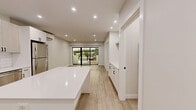 Located at 16 Congress St in Beverly, MA, this thoughtfully designed one-bedroom, three-bathroom unit offers a clean, modern aesthetic with high-quality finishes throughout. Light wood-look flooring flows seamlessly across the entire space, complemented by crisp white walls and recessed lighting that keep the interior bright and airy.

The open-concept kitchen and living area serves as the heart of the unit. The kitchen is well-appointed with two-tone cabinetry — light wood uppers paired with white lowers — stainless steel appliances including a range, microwave, dishwasher, and refrigerator, and a classic white subway tile backsplash. A central island with a white quartz-style countertop provides additional prep and seating space.

The living area features a wall-mounted ductless mini-split system for efficient climate control and access to a private balcony through black-framed sliding glass doors, offering pleasant outdoor views and natural light.

The bedroom is a calm, comfortable retreat, also with sliding glass door access to the balcony. A stylish barn door leads to a dedicated bathroom and in-unit stacked washer/dryer, adding everyday convenience.

The bathrooms showcase a cohesive modern design, featuring floating vanities with integrated sinks, black-framed mirrors, matte black fixtures and hardware, and a sleek glass-enclosed shower. Every detail reflects a commitment to contemporary, functional living.