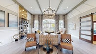 Located at 195 N Creek Dr in Summerville, SC, this single-story clubhouse showcases refined interior design with a welcoming and upscale atmosphere. The entry foyer makes an immediate impression with soaring double-height ceilings, a striking blue accent ceiling detail, decorative pendant lighting, and large-format light tile flooring. A grand arched transom window above the front door floods the entry with natural light, complemented by warm wood-accent wall paneling and an elegantly styled console.

The main lounge area is a standout, featuring exposed painted wood ceiling beams, multiple dramatic iron candelabra chandeliers, and floor-to-ceiling patterned drapery flanking expansive windows that offer views of an outdoor pool area. Rich hardwood-style flooring flows throughout, anchoring an eclectic mix of leather accent chairs, neutral upholstered seating, geometric wood cabinetry, and curated decorative accessories.

A connected lounge and seating nook offers additional gathering space, with wainscoting detail, a gallery wall of landscape artwork, and open metal shelving against a warm wood feature wall. A separate dining area with glass-top tables and upholstered chairs provides a more intimate setting. Throughout the space, layered lighting, thoughtful décor, and an open layout create a cohesive, sophisticated environment ideal for community gatherings.