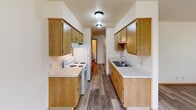 This single-floor unit offers a functional and comfortable layout designed for everyday living. The galley-style kitchen is efficiently organized with warm oak cabinetry lining both walls, providing generous storage space. White appliances, including a range and refrigerator, complement the clean white countertops, while a stainless steel sink and hardwood-look vinyl flooring complete the practical design.

The living area is open and airy, connecting seamlessly to the kitchen via a half-wall partition. Wood-look vinyl flooring extends throughout the common areas, lending a cohesive and easy-to-maintain aesthetic. A window unit air conditioner and baseboard heating ensure year-round comfort, while a large window frames views of lush greenery outdoors.

Two well-sized bedrooms feature plush carpeting and individual windows that invite natural light and garden views. Baseboard heaters in each room provide consistent warmth during cooler months, and vertical blinds offer privacy as needed.

The unit includes two bathrooms. The primary bathroom features a broad vanity with a white countertop sink, oak cabinetry, a well-lit mirror, and a separate water closet. A walk-in closet is also accessible from this area. The second bathroom offers a single-sink vanity with matching oak cabinetry and a combination tub and shower, providing all the essentials in a clean, neutral finish.