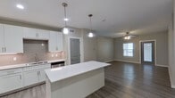 This single-floor residence presents a clean, contemporary design characterized by a neutral gray-and-white color palette and light wood-style luxury vinyl plank flooring that flows consistently throughout the space. The open-concept layout connects the kitchen directly to the living area, creating a cohesive and functional environment.

The kitchen is a standout feature, equipped with a full suite of stainless steel appliances including a refrigerator, range, microwave, and dishwasher. White shaker-style cabinetry extends to the ceiling, providing generous storage, while a tiled backsplash adds subtle texture. A large center island with a white quartz countertop offers additional workspace and casual seating potential. Pendant lights hang above the island, complementing the recessed lighting overhead.

The living area is bright and open, featuring a ceiling fan with integrated lighting and a window that admits natural light. Bedrooms continue the light flooring aesthetic, each fitted with a ceiling fan and window.

Two bathrooms serve the unit. One includes a tub-shower combination with large-format white tile surround, a white vanity, and built-in shelving. The second bathroom features a spacious vanity with a white countertop, wood-style flooring, and marble-effect tile accents. Both bathrooms maintain the unit's consistent modern, minimalist aesthetic.