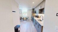 Located at 2024 Jane St in Pittsburgh's South Side neighborhood, this one-bedroom, one-bathroom unit offers a thoughtfully designed layout across a single floor. Light wood-tone flooring runs throughout, lending warmth and visual continuity to the entire space.

The kitchen is a standout feature, outfitted with floor-to-ceiling wood-grain cabinetry accented by matte black hardware, white quartz countertops, and a full suite of stainless steel appliances including a refrigerator, range, over-the-range microwave, and dishwasher. A window at the end of the galley-style kitchen draws in natural light and frames a charming Pittsburgh cityscape, complemented by a compact dining area.

The bedroom is generously proportioned, offering ample room for a full sleeping and living arrangement. A large window provides scenic views of the surrounding Pittsburgh neighborhood, while recessed lighting and a wall-mounted TV add modern convenience. A dedicated workspace with a desk is also incorporated into the room.

The bathroom is clean and contemporary, featuring a wood-grain vanity with a white countertop, an LED-backlit mirror, and a sliding glass walk-in shower with dark hardware accents. The overall design of this unit reflects a cohesive modern aesthetic with practical, well-appointed finishes throughout.