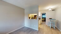 This single-floor unit is thoughtfully laid out to maximize functionality across its key living areas. The living space features light gray walls and wood-style laminate flooring that carries consistently throughout the unit, creating a cohesive and clean aesthetic. A distinctive architectural pass-through window connects the living area to the kitchen, offering an open feel while maintaining defined spaces.

The galley-style kitchen is well-appointed with white shaker cabinetry, dark granite-style countertops, a stainless steel refrigerator, and a black electric range. The contrasting finishes give the kitchen a contemporary look, and the layout makes efficient use of available space.

The unit includes two bedrooms, each featuring wood-style flooring, neutral gray walls, and windows fitted with white horizontal blinds that allow natural light while maintaining privacy. One bedroom includes a closet with sliding doors for storage. Both rooms offer a calm, restful atmosphere.

The bathroom presents a clean, updated design with white cabinetry, dark countertops, an under-mount sink, and a large mirror above the vanity. Light tile flooring complements the overall neutral palette of the unit, contributing to a bright and tidy finish throughout.