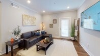 This single-floor residential unit offers a thoughtfully designed layout that balances comfort and functionality. The living room serves as a welcoming central gathering space, featuring crown molding, recessed lighting, warm hardwood-style flooring, and a glass-paneled exterior door that invites natural light. A large sectional sofa and decorative wall art, including a distinctive city map canvas, complete the space with a modern, curated aesthetic.

The kitchen is well-equipped with crisp white shaker cabinets extending to the ceiling, stainless steel appliances including a refrigerator, range, and microwave, and a striking navy blue tile backsplash that adds a bold design accent. Light countertops and an open layout make this kitchen both practical and visually appealing.

The two bedrooms are generously proportioned, each featuring hardwood-style flooring, neutral gray walls, and ample natural light from well-positioned windows. One bedroom includes a mirrored sliding closet door, while both rooms offer a calm, restful atmosphere.

The bathroom is clean and bright, featuring a white vanity with undermount sink, wood-toned flooring, and a shower-tub combination. A mirrored closet adjacent to the bathroom provides additional storage. Throughout the unit, consistent finishes and cohesive décor create a polished, move-in-ready environment.