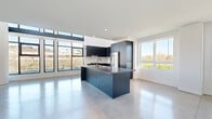 Located at 101 River Park Dr in San Diego's Mission Valley, this contemporary two-story home offers a well-designed layout spread across two floors. The main level is anchored by an open-concept kitchen and living area bathed in natural light from expansive floor-to-ceiling windows. The kitchen features dark, fluted-panel cabinetry, a large center island with a waterfall-edge countertop and integrated sink, stainless steel appliances, and polished concrete floors that extend seamlessly throughout the main level. The living area is generously proportioned, with views of the surrounding greenery and park through large picture windows and a glass-panel outdoor staircase. The upper level houses both bedrooms, each finished with warm hardwood flooring and bright windows overlooking the neighborhood and parkland. The primary bedroom is well-sized and accompanied by a walk-in closet outfitted with custom built-in shelving, hanging rods, and drawers. Both bathrooms are finished consistently with the home's modern aesthetic, featuring dark fluted vanity cabinetry, backlit mirrors, and clean-lined fixtures. A dedicated staircase connects the two floors, and a closet provides additional storage. The exterior reveals a compact modern structure with large glazed facades and an outdoor staircase leading to a landscaped green area.