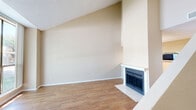 This well-designed two-story residence offers one bedroom and two full bathrooms across a thoughtfully arranged floor plan. The main level features an open living area distinguished by soaring vaulted ceilings that create an impressive sense of vertical space. A classic fireplace with a white mantle and tile surround serves as the focal point of the living room, which is finished with warm hardwood-style flooring throughout. A large sliding glass door floods the space with abundant natural light while providing direct views of mature trees and lush greenery outside. The kitchen is efficiently laid out with white cabinetry, light countertops, a double sink, and black appliances including a range, microwave, and refrigerator. A peninsula counter connects the kitchen to a dining or hallway area, enhancing the open flow of the main level. A full bathroom on this floor features a tub/shower combination with white tile surround. Upstairs, the generously sized primary bedroom features plush carpeting, a built-in desk area, and direct access to a well-appointed en suite bathroom with a wide vanity, ample cabinetry, and a lighted mirror. The upper level also includes a dedicated closet. Throughout the home, neutral warm tones and textured ceilings contribute to a clean, move-in-ready ambiance.