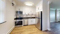 This well-appointed single-floor unit in Downers Grove, IL presents a thoughtfully designed layout comprising one bedroom, one bathroom, and a fully equipped kitchen. Throughout the space, warm hardwood-style flooring provides a cohesive aesthetic, complemented by crisp white trim, crown molding, and neutral gray walls that create a clean, modern atmosphere.

The bedroom features a distinctive paneled ceiling with a ceiling fan, crown molding, and a window that allows natural light to fill the room. A baseboard heating system ensures year-round comfort. The open living and kitchen area shares a similar design, with an additional ceiling fan and window providing ventilation and natural light.

The kitchen is notably well-appointed, featuring white shaker-style cabinetry, dark granite countertops, a mosaic tile backsplash, and a full suite of stainless steel appliances including a range, microwave, dishwasher, and refrigerator. The hardwood-style flooring continues seamlessly throughout this area.

The bathroom is finished in a bright, contemporary style with large-format tile flooring, subway tile wainscoting, a tiled walk-in shower with a glass door, a white vanity, and a narrow frosted window for natural light and privacy. Baseboard heating is present here as well, ensuring consistent warmth throughout the entire unit.