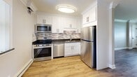 This well-appointed single-floor unit in Downers Grove, IL presents a thoughtfully designed layout comprising one bedroom, one bathroom, and a fully equipped kitchen. Throughout the space, warm hardwood-style flooring provides a cohesive aesthetic, complemented by crisp white trim, crown molding, and neutral gray walls that create a clean, modern atmosphere.

The bedroom features a distinctive paneled ceiling with a ceiling fan, crown molding, and a window that allows natural light to fill the room. A baseboard heating system ensures year-round comfort. The open living and kitchen area shares a similar design, with an additional ceiling fan and window providing ventilation and natural light.

The kitchen is notably well-appointed, featuring white shaker-style cabinetry, dark granite countertops, a mosaic tile backsplash, and a full suite of stainless steel appliances including a range, microwave, dishwasher, and refrigerator. The hardwood-style flooring continues seamlessly throughout this area.

The bathroom is finished in a bright, contemporary style with large-format tile flooring, subway tile wainscoting, a tiled walk-in shower with a glass door, a white vanity, and a narrow frosted window for natural light and privacy. Baseboard heating is present here as well, ensuring consistent warmth throughout the entire unit.