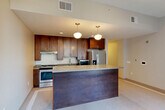 Located in the heart of downtown Detroit on Griswold Street, this one-bedroom, one-bathroom residence offers a thoughtfully designed single-floor layout. The open-concept living, dining, and kitchen area serves as the centerpiece of the home, creating a seamless flow ideal for both everyday living and entertaining. The kitchen is equipped with rich, dark-stained wood cabinetry, stainless steel appliances including a refrigerator and microwave, a gas range, and a large peninsula with a smooth countertop surface illuminated by stylish pendant lighting overhead. Tile flooring runs throughout the main living areas, lending a clean, contemporary feel. A bright hallway connects the living space to the private quarters, lined with flush-mount drum lighting and access to two closets and an in-unit laundry area. The bedroom features soft carpeting and neutral tones, offering a comfortable retreat. The bathroom is finished with a floating wood vanity, a mirrored medicine cabinet, tile flooring with mosaic accents, and clean, minimal fixtures. A dedicated living area at the end of the hallway boasts large windows framing striking views of the Detroit skyline, filling the space with abundant natural light.