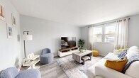 The Gilmore Renovated unit in Largo, Florida offers a thoughtfully updated single-floor layout comprising a living room, dining area, kitchen, bedroom, bathroom, hallway, and closet. Light gray walls and wood-look luxury vinyl flooring flow throughout the main living areas, creating a clean, cohesive aesthetic.

The living room is bright and welcoming, featuring a large window dressed with sheer curtains that allow natural light to fill the space. The adjacent dining area connects seamlessly to the kitchen, providing an open and functional flow ideal for everyday living.

The galley-style kitchen is well-appointed with crisp white cabinetry, stainless steel appliances including a refrigerator, range, and dishwasher, and a single-basin sink with modern fixtures. The layout maximizes efficiency while maintaining a bright, contemporary feel.

The generously sized bedroom is finished with plush wall-to-wall carpet, vertical blinds offering privacy, a ceiling fan with light fixture for year-round comfort, and a built-in closet with bi-fold doors providing ample storage.

The bathroom features a white vanity with updated hardware, a large mirror, modern light bar, and a tiled tub/shower combination, all finished with wood-look tile flooring for a polished look. This renovated unit combines practicality with modern design throughout.