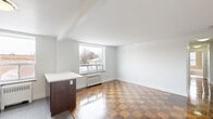 Located at 1065 Eglinton Ave W in Toronto's vibrant midtown neighbourhood, this 2-bedroom, 1-bathroom unit offers a practical and well-appointed layout across a single floor. The combined kitchen and living area serves as the heart of the space, featuring a striking checkerboard-patterned parquet hardwood floor that extends throughout most of the unit. The updated kitchen is equipped with stainless steel appliances — including a range, microwave, and dishwasher — dark espresso cabinetry, a tiled backsplash, and a peninsula with a white countertop that doubles as a breakfast bar. Large windows in the living area allow generous natural light to fill the space and provide views of the surrounding neighbourhood. Both bedrooms continue the parquet flooring and are finished with crisp white walls and clean baseboards. The primary bedroom benefits from a large window with a radiator beneath it, offering views of the streetscape. The bathroom is finished with full-height beige subway tile surrounding a soaker tub and shower, complemented by a white vanity and a frosted privacy window. A hallway connects the rooms, completing the efficient and functional floor plan.