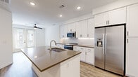This well-designed 2-bedroom, 1-bathroom unit in Centennial, CO offers a clean, modern aesthetic across a single floor. The open-concept kitchen and living area serves as the heart of the home, anchored by a large center island with a quartz countertop, undermount sink, and built-in dishwasher. White shaker cabinetry reaches toward the ceiling, complemented by a white subway tile backsplash and a full suite of stainless steel appliances, including a refrigerator with ice and water dispenser, electric range, and microwave. Wood-look plank flooring flows throughout the living areas, adding warmth to the bright, white interior lit by recessed lighting and a ceiling fan. The spacious primary bedroom features a ceiling fan, natural light from a large window, and access to a generous walk-in closet with built-in shelving and hanging rods. The second bedroom includes a glass-panel door opening to a private balcony with exterior views. The bathroom is finished with white cabinetry, quartz countertops, and tile flooring. A dedicated in-unit laundry area with a stacked washer and dryer provides added convenience. The unit's clean lines and neutral palette create a bright, functional living environment.