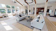 Located at 1220 Crawford Ct in Granbury, Texas, this exceptional single-story lakefront home blends rustic Texas charm with refined modern design. The expansive open-concept living area commands attention with soaring vaulted ceilings adorned with rich wood beams, dramatic limestone columns, and light hardwood flooring that flows seamlessly throughout. A striking wrought-iron chandelier anchors the great room, where two generous seating areas invite relaxed gathering. A floor-to-ceiling limestone fireplace serves as a focal point, framed by large windows that open to sweeping lake views and lush outdoor greenery. The dining area is bathed in natural light from an impressive wall of windows overlooking the waterfront, offering panoramic views that create a serene backdrop for any occasion. The kitchen features a bold reclaimed wood accent wall with open shelving, a white island with bar seating, and pendant lighting that adds warmth and character. Throughout the home, the interplay of natural stone, aged wood, and crisp white walls creates a cohesive coastal-farmhouse aesthetic. The overall ambiance is bright, airy, and welcoming, with every principal space thoughtfully oriented to maximize the stunning lakefront setting.