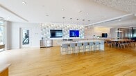 Located along the scenic Revere Beach Boulevard in Revere, MA, this expansive single-floor space offers a generously sized, open-concept layout bathed in natural light from floor-to-ceiling windows that frame breathtaking ocean views. Warm hardwood flooring flows throughout, tying together a series of distinct yet connected areas.

The game room is a standout feature, centered around a full-size billiards table beneath a contemporary chandelier, with textured stone-clad columns and ceiling accents lending architectural character. Adjacent lounge areas are elegantly appointed with plush sofas, accent chairs, and vivid artwork, all oriented to take full advantage of the sweeping beachfront vistas.

A sleek, modern kitchen anchors one end of the space, boasting a large island with bar seating, pendant lighting, dual mounted flat-screen televisions, and a bold geometric-tiled feature wall. The entry corridor is defined by beautifully crafted wood panel wall detailing and recessed lighting, creating a polished first impression.

Throughout, the design aesthetic is sophisticated and cohesive, blending neutral tones with coastal-inspired accents of blue and teal. The abundance of natural light, open sightlines, and carefully curated furnishings combine to create a bright, welcoming, and highly functional environment.