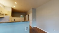 Located along S River Pkwy in Portland, Oregon, this single-floor apartment offers a practical and well-appointed layout with consistent hardwood-style flooring running throughout. The entry area welcomes natural light through a large window fitted with blinds, complemented by a ceiling fan with integrated lighting and a wall-mounted mini-split system for efficient climate control.

The open-concept kitchen and living area forms the heart of the unit. A peninsula with granite countertops and a raised breakfast bar separates the kitchen from the living space. The kitchen itself is equipped with white cabinetry, a granite countertop with an undermount sink, a coil-top range, a built-in microwave, and a full-size refrigerator—all finished in white. A wall-mounted heater is integrated into the base of the peninsula.

The bathroom features a dark countertop vanity with white cabinetry, a round mirror, and a window for natural light. Notably, in-unit laundry—including a full-size washer and dryer—is housed in a dedicated closet alongside the water heater, adding significant convenience. The overall color palette of soft gray walls and white trim gives the space a clean, neutral character throughout.