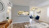 This single-floor residence offers a thoughtfully designed layout that balances comfort and functionality. The open-concept living and dining area is anchored by warm wood-look flooring and bathed in natural light streaming through large windows dressed with sheer white curtains. A ceiling fan overhead adds both style and practicality to the space. The living area flows seamlessly into the dining zone, creating an inviting environment for everyday living and entertaining.

The kitchen is defined by a distinctive pass-through window framed by a gray accent wall, allowing for easy interaction between the kitchen and main living areas. Inside, the kitchen features white cabinetry, a double-basin stainless steel sink, crisp white countertops, and a stylish subway-tile mosaic backsplash in neutral tones that adds a contemporary touch.

The bedroom is a serene retreat with plush carpeting, a large window that invites natural light, and access to a generously sized walk-in closet outfitted with wire shelving on both sides — offering ample storage. The bathroom is clean and functional, featuring wood-look flooring, a tub-shower combination, and a vanity with storage.

Throughout the space, textured ceilings and clean white walls provide a neutral backdrop that complements any décor style.