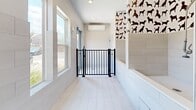 This dedicated pet wash and grooming hallway is thoughtfully designed with both functionality and charm in mind. The space is finished with large-format, light-toned tile along the walls and a pale tile floor that is easy to clean and maintain. A standout feature is the eye-catching wallpaper adorning the upper portion of the wash area, showcasing silhouettes of various dog breeds in warm brown and black tones against a white background, lending the space a welcoming, pet-friendly character.

The grooming station includes a built-in bathing tub equipped with a wall-mounted faucet and flexible sprayer hose, making pet bathing convenient and efficient. Adjacent to the tub, rich warm-toned cabinetry with sleek hardware provides ample storage for grooming supplies and accessories. A black iron safety gate spans the width of the hallway, ensuring pets remain securely within the wash area during use.

Climate control is handled by a wall-mounted mini-split unit, keeping the space comfortable year-round. Large windows along one wall allow natural light to fill the room, creating a bright and airy atmosphere. Recessed ceiling lighting provides additional illumination. Overall, this space is a well-appointed, practical, and visually engaging pet care area.