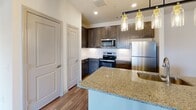 This single-story, two-bedroom, two-bathroom residence in Austin, Texas offers a thoughtfully designed open-concept layout with a clean, contemporary aesthetic. The kitchen serves as a central focal point, featuring dark espresso cabinetry, granite countertops, stainless steel appliances including a refrigerator, electric range, and microwave, along with a kitchen island with an integrated sink. Pendant lighting over the island adds a polished touch, while wood-style flooring extends throughout the main living areas.

The living area is bright and open, benefiting from natural light that enters through French doors leading to an outdoor balcony area, complemented by a ceiling fan overhead. Both bedrooms are carpeted for comfort, with ceiling fans and windows providing natural light and outdoor views. Each bedroom includes access to a closet, with at least one featuring a walk-in configuration.

The two bathrooms are finished consistently with dark cabinetry, granite-topped vanities, wood-style flooring, and glass-enclosed showers. Additional storage cabinetry is present in both bathrooms. The overall palette of neutral tones throughout creates a clean, cohesive environment well-suited for a variety of furnishing styles.