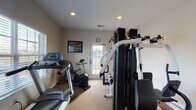 Located at 200 Gallery Dr in Marysville, Ohio, this single-floor fitness facility offers a dedicated and functional space designed to support a full range of exercise activities. The primary workout room is well-appointed with a variety of equipment, including a treadmill, a stationary recumbent bike, and a multi-station cable weight machine, providing options for both cardiovascular and strength training. Recessed ceiling lighting illuminates the carpeted floor, while a textured ceiling adds a classic finish to the room. A door with a window at the far end of the exercise room allows natural light to filter in and provides direct access to the outdoors, contributing to an open and welcoming atmosphere. Framed artwork on the walls adds a touch of character to the practical space. Additional rooms visible in the space, though dimly lit, appear to include utility or support areas featuring windows with blinds, offering further versatility. Overall, this facility presents a straightforward, well-equipped environment well-suited for regular fitness use.