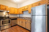 Located on West 14th Street in Chattanooga, Tennessee, this single-floor unit offers a functional and straightforward layout with a cohesive design throughout. The kitchen is well-equipped with stainless steel appliances, including a range with oven, dishwasher, and refrigerator. Warm-toned oak cabinetry provides ample storage, complemented by dark granite-style countertops and a double-basin sink. Track lighting illuminates the workspace, and the kitchen opens conveniently toward the main living area. Hardwood-style flooring runs consistently through the kitchen and living spaces, lending warmth and visual continuity to the unit. The living area features neutral gray walls, a large window allowing natural light and street views, and multiple electrical outlets positioned for flexible furniture arrangements. The bathroom carries a classic aesthetic, with a black-and-white checkered tile floor and a matching checkerboard accent border running along the tub surround. White subway-style tiles line the full tub and shower combination, which also includes a grab bar for added accessibility. A wood-toned vanity with a dark countertop completes the space. Overall, the unit presents a clean, practical interior suited to everyday living.