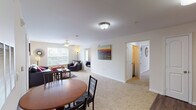 This single-floor residence offers a well-organized layout that balances communal living spaces with private retreats. The open-concept living and dining area forms the heart of the unit, where soft carpet flooring, ceiling fans, and natural light from multiple windows create a comfortable and inviting atmosphere. A round dining table sits adjacent to the living room, which provides ample space for seating and relaxation.

The kitchen is efficiently designed with warm oak cabinetry extending to the upper walls, providing generous storage. Black appliances, including an electric range, over-the-range microwave, dishwasher, and refrigerator, are paired with light countertops and a single-basin sink. Wood-style flooring runs throughout the kitchen, adding a practical, durable surface.

The unit includes multiple bedrooms, each carpeted and equipped with ceiling fans. The bedrooms receive natural light through windows with views of surrounding greenery. Two bathrooms serve the unit, each featuring a tub-shower combination, wood-style flooring, and oak vanity cabinetry. The overall design is clean and neutral, offering a functional and comfortable living environment throughout.
