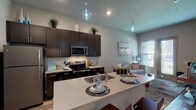 Located in Twin Oaks, MO, this single-floor residence showcases a thoughtfully designed open-concept layout with modern finishes throughout. The kitchen is a standout feature, equipped with dark espresso cabinetry, stainless steel appliances including a refrigerator, microwave, and range, complemented by a tiled backsplash and a large quartz-topped island with an undermount sink and bar seating. Stylish pendant lighting hangs above the island, adding a contemporary touch. The kitchen flows seamlessly into the living area, where natural light pours through large windows and a glass-paneled door leading to an outdoor view. The living space is accented by elevated ceilings that enhance the sense of openness. Two bedrooms provide comfortable accommodations, each featuring carpeted flooring, generous windows, and ample natural light. A walk-in closet with wire shelving connects to a full bathroom with a shower-tub combo. A second bathroom features a single-sink vanity with dark cabinetry, a large mirror, and wood-look flooring. Throughout the residence, light hardwood-style floors in the main areas and neutral gray tones on the walls create a cohesive, contemporary aesthetic that is both functional and visually appealing.