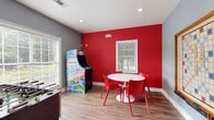 Located in McDonough, Georgia, this single-floor game room is designed for entertainment and social interaction, combining bold design choices with a well-curated selection of recreational amenities. The space features a striking color palette, with a vivid red accent wall contrasting against cool gray walls, creating an energetic yet cohesive atmosphere throughout.

The wood-look flooring runs seamlessly across the room, grounding the space with warmth and durability. Natural light filters in through multiple windows fitted with white blinds, offering views of surrounding greenery and keeping the room bright and inviting.

A standout Arcade Legends multi-game cabinet anchors one corner of the room, providing classic gaming entertainment. Nearby, a full-size foosball table offers competitive fun and serves as a central activity hub. A wall-mounted oversized Scrabble board with an adjacent chalkboard adds a creative, interactive element to the décor while encouraging group play.

A round white pedestal table surrounded by bold red chairs provides a casual seating and gathering area, ideal for tabletop games or conversation. Recessed lighting supplements the natural light, ensuring the space remains well-lit at all times.

Overall, the room balances playful energy with thoughtful design, making it a dynamic and engaging space for recreation and socializing.