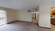 This single-floor unit at 64 Gahl Terr in Reading, Ohio offers a practical and well-organized layout designed for comfortable everyday living. The living area is generously proportioned, finished with neutral-toned carpet and cream-colored walls that create a bright, open atmosphere. A sliding glass door with vertical blinds fills the space with natural light while providing access to an outdoor area, making it a welcoming central gathering space. The kitchen is equipped with warm oak-toned cabinetry offering ample storage, gray laminate countertops, a white electric range, dishwasher, and a double-basin sink. The tile flooring adds durability and easy maintenance to this functional cooking space. A hallway connects the main living area to the private quarters, which include multiple carpeted bedrooms, each featuring textured ceilings, neutral walls, and windows with blinds that allow for natural light and privacy. Dark wood baseboards provide a consistent design detail throughout the unit. The bathroom is cleanly appointed with a wood-toned vanity, white countertop, a tub-shower combination with tiled surround, and matching tile flooring. Overall, the unit presents a clean, functional, and move-in ready environment suited for a range of occupants.