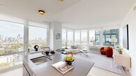 Located at 421 Summit Ave in Jersey City, NJ, this two-bedroom residence offers a thoughtfully designed open-concept layout that maximizes both space and natural light. The combined kitchen and living area serves as the heart of the home, anchored by expansive floor-to-ceiling windows on multiple walls that frame breathtaking views of the Jersey City and Manhattan skylines. The living room features light hardwood flooring and ample space for comfortable seating arrangements, seamlessly flowing into the dining area.

The kitchen is outfitted with sleek two-tone cabinetry in natural wood and deep navy, stainless steel appliances, a large island with a built-in sink and seating for two, and a window overlooking the city — making it as functional as it is stylish.

The primary bedroom is generously proportioned, bathed in natural light through large windows that continue the skyline views, and features light wood flooring. The second bedroom is equally bright, with large windows and clean white walls. Both rooms benefit from dedicated closet space. Throughout, the residence maintains a crisp, modern aesthetic with white walls, contemporary finishes, and an airy ambiance that reflects the elevated urban setting.