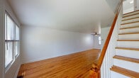 Located at 283 Cooper Pl in New Haven, CT, this three-floor home is designed for practical, comfortable living. The main level features warm hardwood flooring that flows throughout an open living area, where a classic staircase with wooden balusters and white spindles serves as a central architectural element. Natural light filters in through multiple windows, and ceiling fans provide added comfort. The updated kitchen is well-appointed with dark granite countertops, white shaker-style cabinetry, stainless steel appliances including a refrigerator, gas range, and dishwasher, along with a dedicated open pantry for additional storage. A clean, white full bathroom features tile flooring, a tub-shower combination, and a single vanity. The upper floor offers an expansive open room with vaulted ceilings and a ceiling fan, ideal as a primary bedroom or flexible living space, with views of the surrounding greenery. Additional bedrooms on the second floor are bright and airy, each with hardwood floors and natural light from exterior windows. The basement level provides practical utility space, housing a full-size washer and dryer, exposed structural beams overhead, and a separate window for ventilation, making it a functional laundry and storage area.