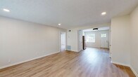 This single-floor space has been carefully updated with a clean, modern aesthetic that flows seamlessly from room to room. Light hardwood-style flooring runs throughout, creating a cohesive and airy feel across the entire layout.

The kitchen is a standout feature, showcasing gray shaker-style cabinetry with matte black hardware, crisp white countertops, and a hexagonal tile backsplash that adds a contemporary touch. Open natural wood shelving with black iron brackets provides functional display space, while stainless steel appliances — including a refrigerator, range, and dishwasher — complete the well-equipped cooking area. A single-basin stainless steel sink with a brushed nickel faucet anchors the counter space.

The kitchen opens into a bright, open living area bathed in natural light from multiple windows fitted with white blinds. A classic paneled front door with a glass insert adds charm to the entry. Recessed lighting and a textured ceiling lend character to the living space, which connects to additional rooms via open doorways.

The bedroom offers a comfortable, sunlit retreat with dual windows overlooking the surrounding neighborhood and a sleek ceiling fan for year-round comfort. Neutral wall tones and clean trim work throughout give the entire space a fresh, move-in-ready appeal.